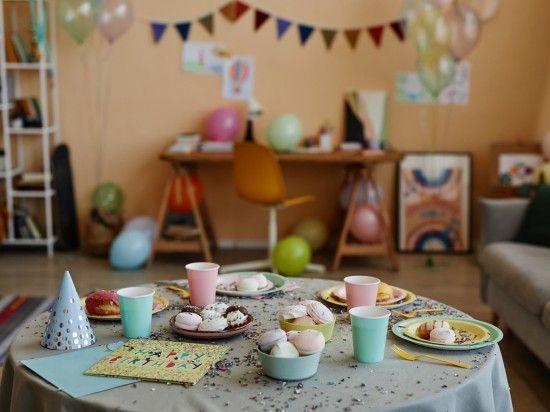 Przyozdobiony dom na urodziny dziecka. Na stole są ciastka i odpowiednie dekoracje. W tle balony.