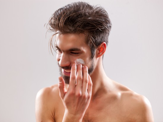 Uśmiechnięty mężczyzna smaruje policzek kremem do twarzy