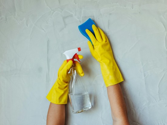 Dłonie rękawicach zmywają ścianę za pomocą gąbki oraz płynu wg. wskazówek znalezionych w aplikacji do sprzątania.