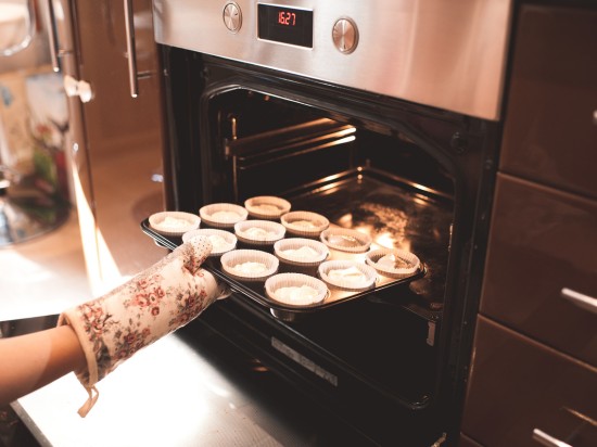 Ręka w ochronnej rękawicy wyjmuje upieczone ciastka z piekarnika.