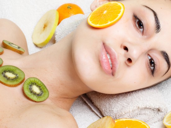 Kobieta leży i ma nałożone na twarz i szyję kiwi oraz plastry pomarańczy