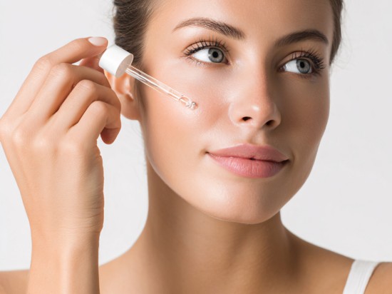 Kobieta nakłada na twarz serum z kwasami PHA przy pomocy pipety.
