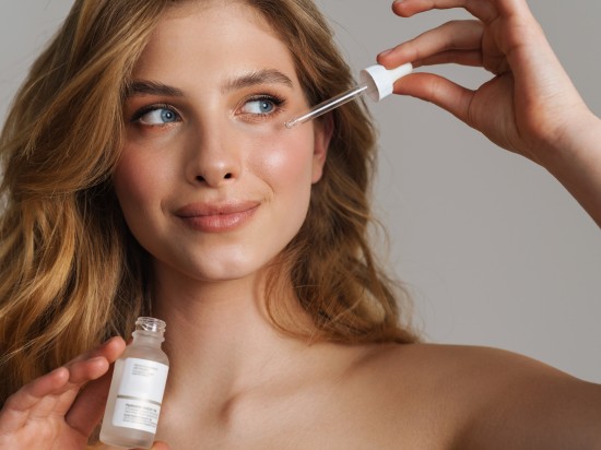 Uśmiechnięta kobieta nakłada na policzek serum do twarzy z bakuchiolem.