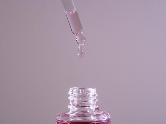 Szklana pipeta dozująca serum do twarzy z bakuchiolem na fioletowym tle.