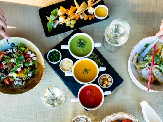 Dwie osoby jedzą wspólny posiłek. Na stole jest wiele potraw zawierających dużo warzyw.