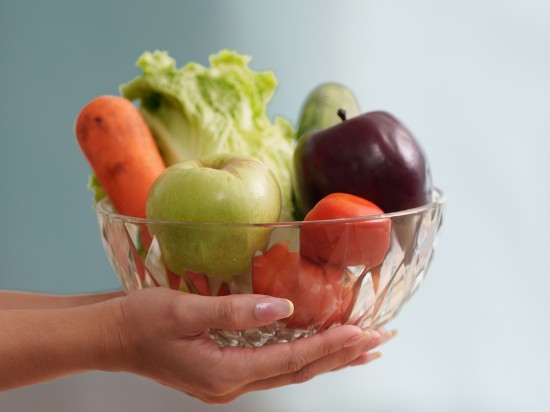 Kobiece dłonie trzymają miskę owoców oraz warzyw symbolizujące dobre nawyki żywieniowe.