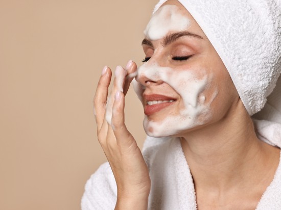 Kobieta w turbanie na głowie oczyszcza pianką twarzy aby uniknąć wągrów i zaskórników.