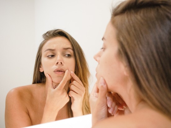 Kobieta stoi przed lustrem i próbuje manualnie usunąć wągry i zaskórniki w domu.