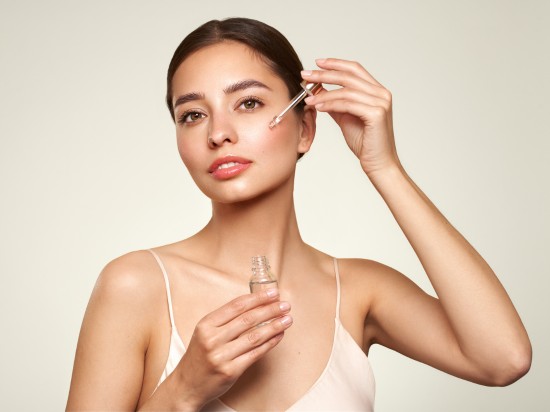 Kobieta nakładająca pipetą serum do twarzy na jasnym tle