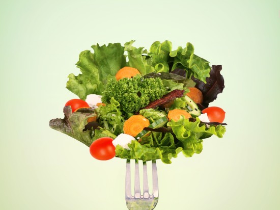 Sałata i inne warzywa takie jak marchewka, pomidor nadziane na widelec symbolizujące zdrowe odżywianie.