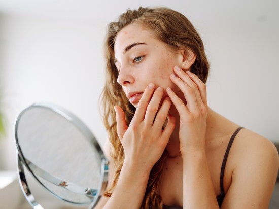 Kobieta siedzi przed lustrem i sprawdza efekty dbania o swoją cerę.