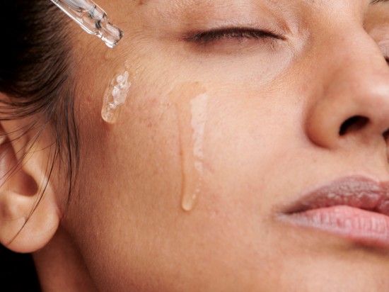 Kobieta nakłada na twarz serum przy pomocy szklanej pipety