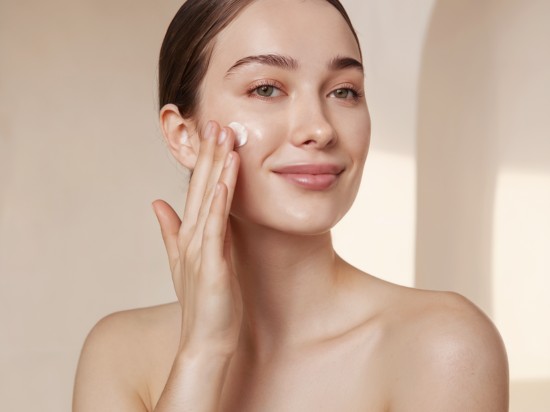 Uśmiechnięta kobieta nakłada na policzek krem do twarzy