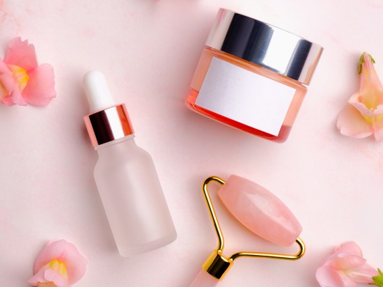 Krem do twarzy, serum oraz masażer z kamienia na różowym tle z kwiatkami