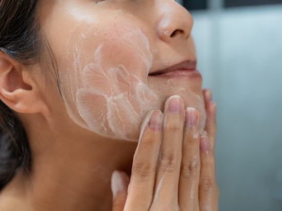 Kobieta przy pomocy pianki do mycia twarzy czyści skórę.