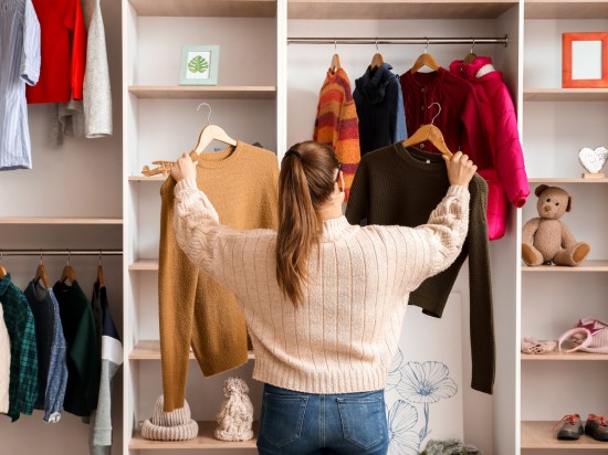 Kobieta przegląda ubrania w swojej szafir i próbuje zorganizować je w duchu szafy kapsułowej.