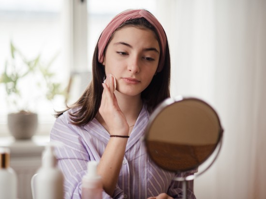 Nastolatka siedzi przed lustrem i wacikiem tonizuje skórę