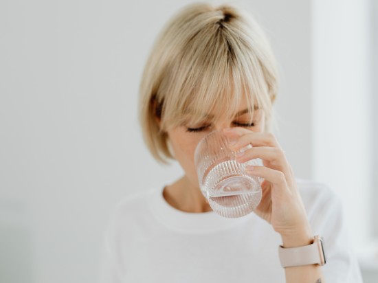 Kobieta pije szklankę czystej wody utrzymując w ten sposób odpowiedni poziom nawodnienia.