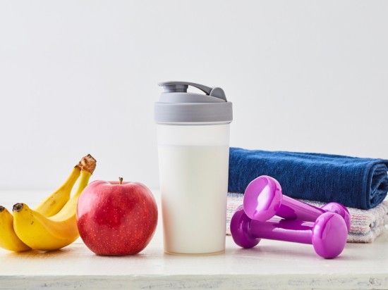 Na stole leżą owoce, hantle do ćwiczeń, koktajl symbolizujące zdrowy tryb życia.