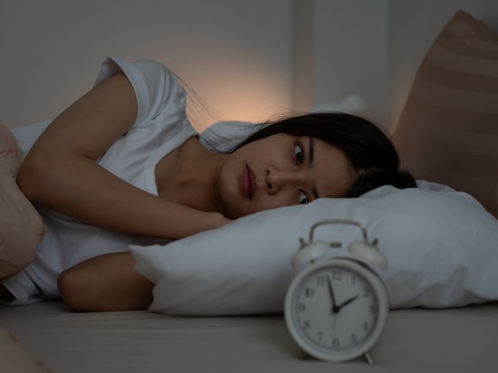 Kobieta leżąca w łóżku patrząca na budzik – bezsenność.