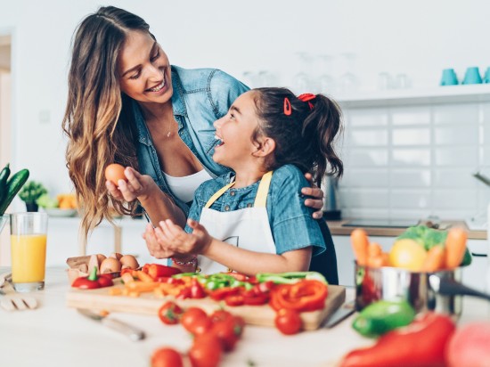 Matka z córką śmieją się do siebie podczas wspólnego gotowania obiadu, który wspiera zdrowe nawyki w rodzinie.