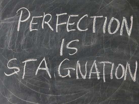 Napis „Perfection is stagnation” zapisany kredą na tablicy.