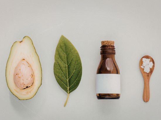 Awokado, liść ziołowy, syrop oraz łyżka z przyprawami leżą na stole.