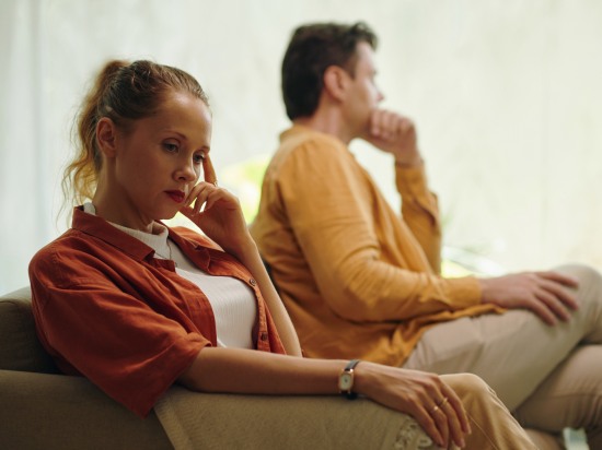 Para siedząca osobno na kanapie – napięcie w relacji.