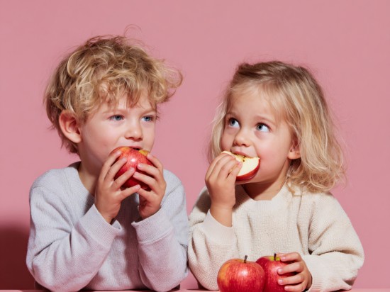 Dwójka małych dzieci je zdrową przekąskę w postaci jabłka.