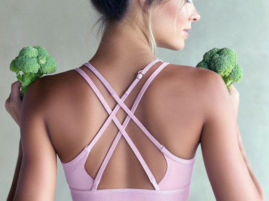 Kobieta w sportowym stroju do ćwiczeń trzyma dwa brokuły symbolizujące zdrowe nawyki.