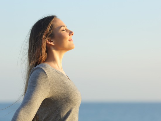 Uśmiechnięta kobieta stoi o poranku na świeżym powietrzu i ćwiczy oddech.