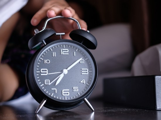 Osoba próbuje zgasić o poranku dzwoniący budzik na pobudkę.