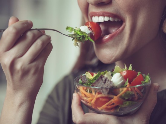 Uśmiechnięta kobieta stosuje trend mindful eating - je na przekąskę zdrową sałatkę z warzyw.