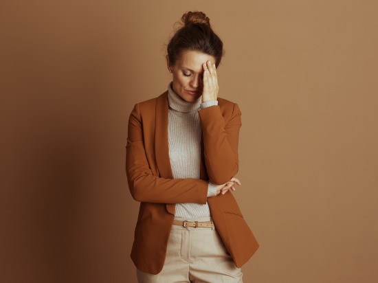Zestresowana kobieta w biurowym stroju stoi i trzyma się za głowę. Próbuje poradzić sobie ze stresem.