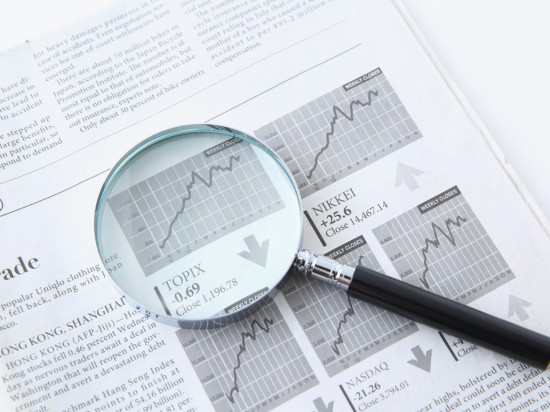 Gazeta z wynikami giełdy, na której leży lupa.