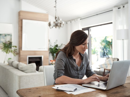 Kobieta siedzi przed komputerem i podlicza rachunki domowe planując wydatki.