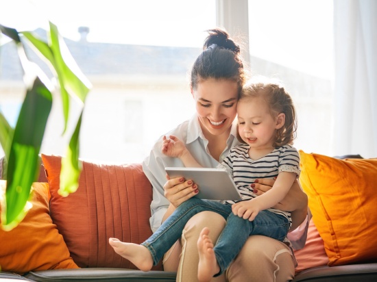 Kobieta z dzieckiem na kanapie przegląda tableta.